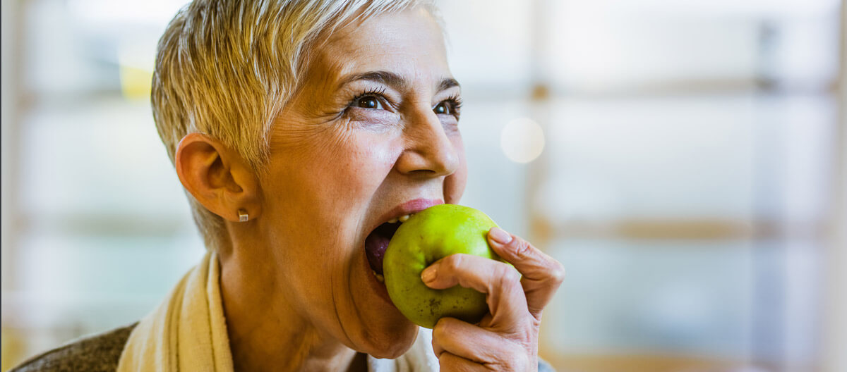 Seniorin beißt in einen Apfel – gesundes Zahnfleisch nach der Parodontitis-Behandlung