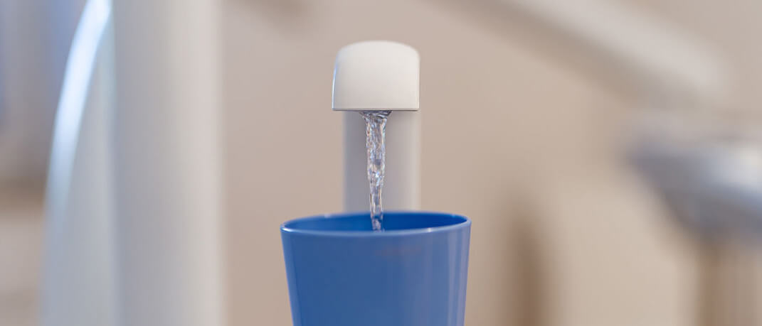 Wasser fließt an der Behandlungseinheit in einen Becher – geprüfte Wasserhygiene